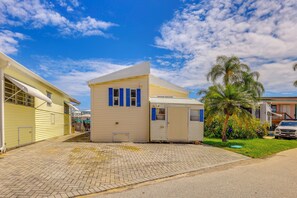 Um edifício de dois andares com garagem, uma pequena construção anexa e uma palmeira no quintal.