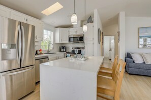 A modern kitchen with stainless steel appliances, a central island, and a dining area with wooden chairs. - Resort-Style Living! Waterfront Nettles Island Gem (Jensen Beach)