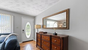 Een kamer met een houten dressoir, een spiegel, een lamp en een raam met jaloezieën.