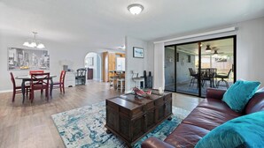 Een woonkamer met een eethoek, een salontafel, een bank en een groot raam.