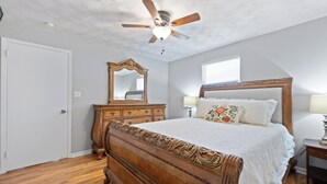 Een slaapkamer met een houten bed, een plafondventilator, een dressoir en een spiegel.