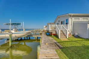 Un port de plaisance avec des bateaux amarrés, une promenade en bois et une rangée de maisons blanches bordées d’une pelouse verdoyante.