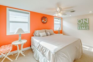 A bedroom with a bed, a ceiling fan, a window, a wall-mounted lamp, a small table, a bench, and a 'ON BEACH TIME' sign. - Kim G's Bayside Cottage: Montego Bay (Ocean City)