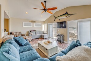 A living room with a ceiling fan, a large fish decoration, a sofa, a coffee table, and a television. - Kim G's Bayside Cottage: Montego Bay (Ocean City)