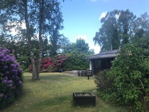 A garden with a wooden structure, a grassy lawn, and trees.