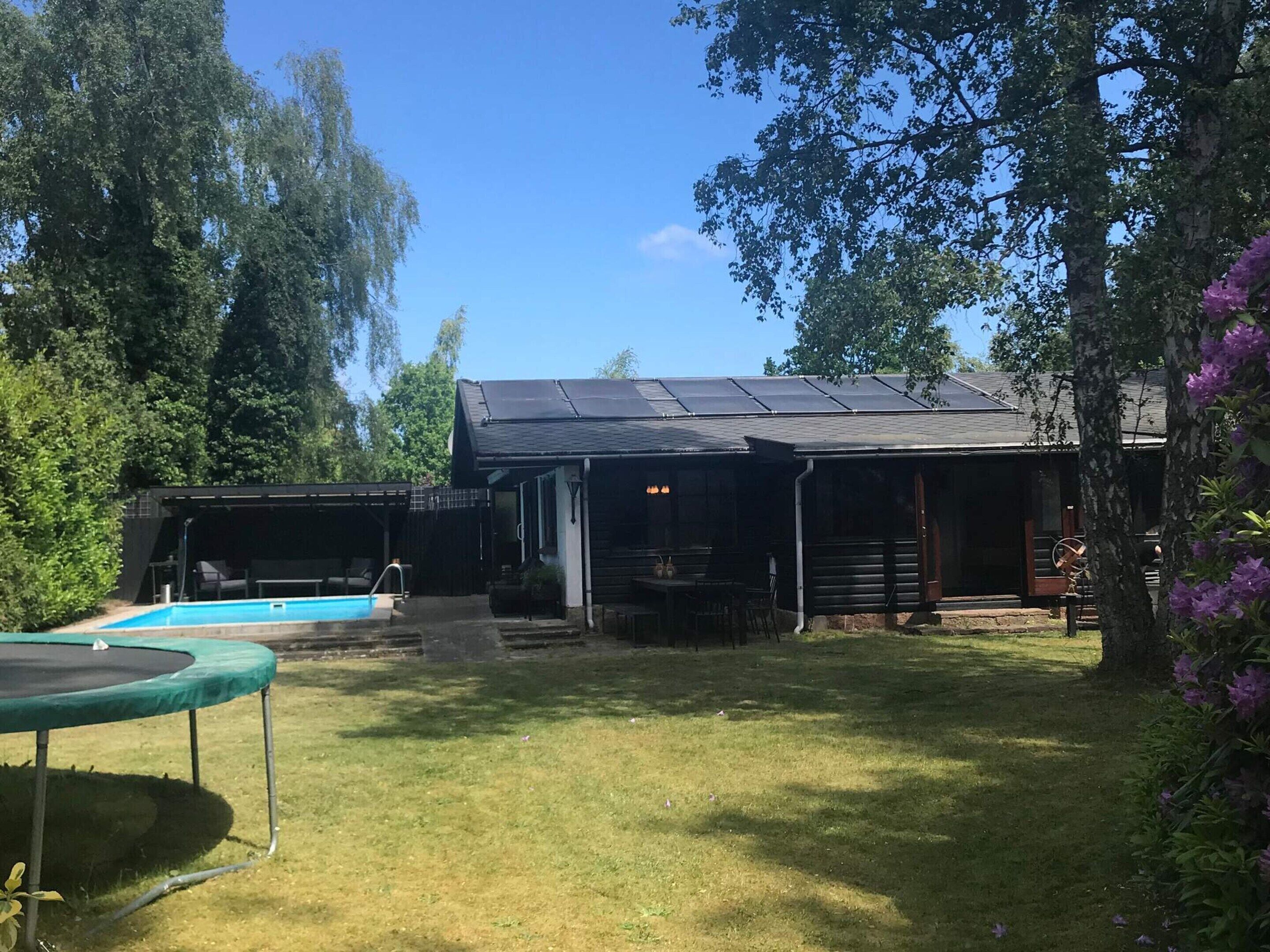 Et hus med swimmingpool, overdækket terrasse og solpaneler på taget.