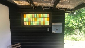 En träbänk, en brevlåda och ett fönster med en utsmyckning i färgat glas.