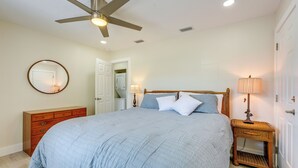 Un dormitorio con cama, ventilador de techo, mesita de noche con lámpara, cómoda y espejo.