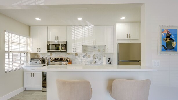Una cocina moderna con armarios blancos, una isla central con taburetes altos, un microondas y un refrigerador.