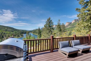 A deck with a grill, lounge chairs, and a scenic view of a lake and mountains.