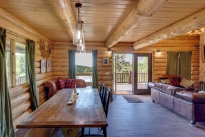 L’intérieur d’une cabane en rondins, avec une table à manger en bois, des sièges en cuir et une vue à travers une porte vitrée.