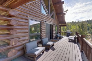 A log cabin with a deck, outdoor seating, and a view of the forest.