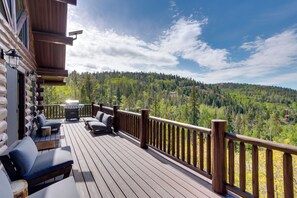 A wooden deck with outdoor seating, a barbecue grill, and a view of a forested mountain.