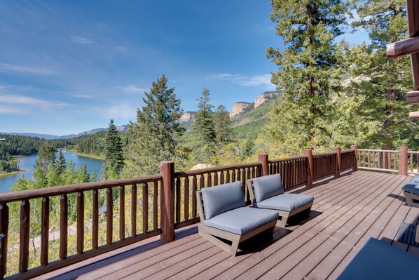 A wooden deck with two lounge chairs, overlooking a lake and forested mountains.