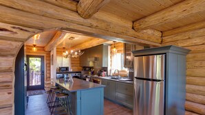 Een keuken in een blokhutstijl met een centraal eiland, barstoelen, roestvrijstalen apparatuur en een houten plafond.