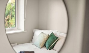 Ein Zimmer mit Fenster, einem Bett mit Kissen und Blick ins Grüne.