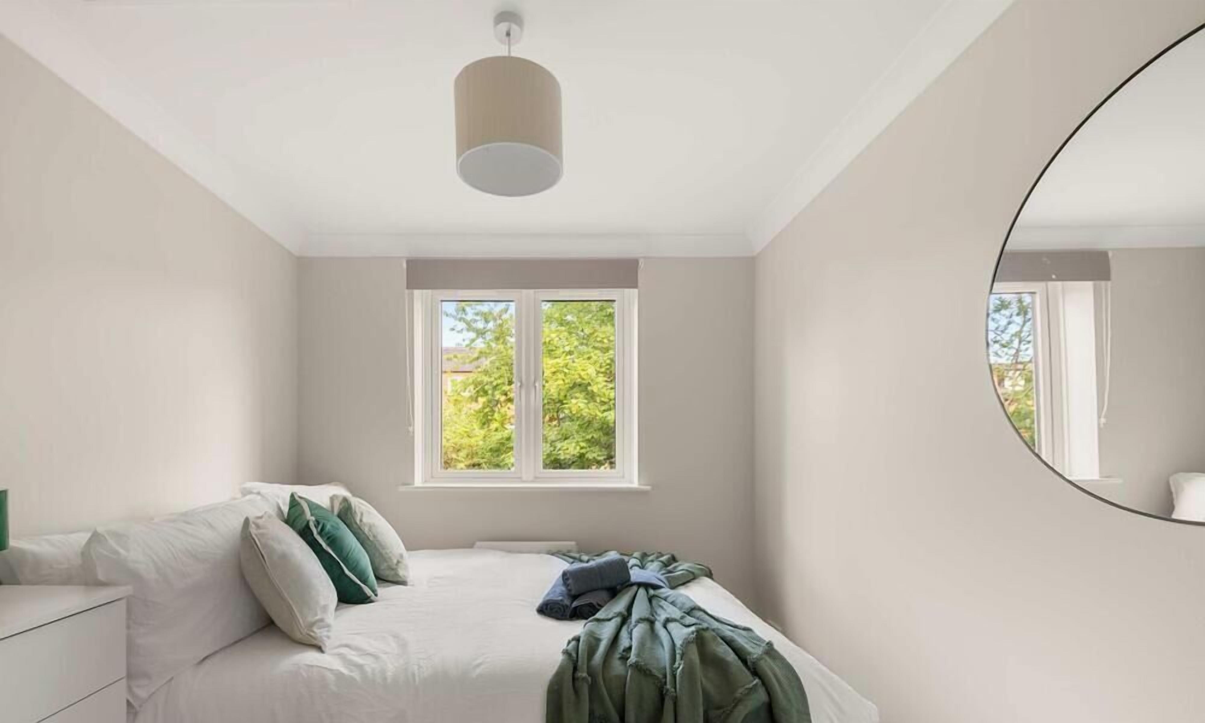 A bedroom with a bed, a window, a mirror, and a ceiling light.