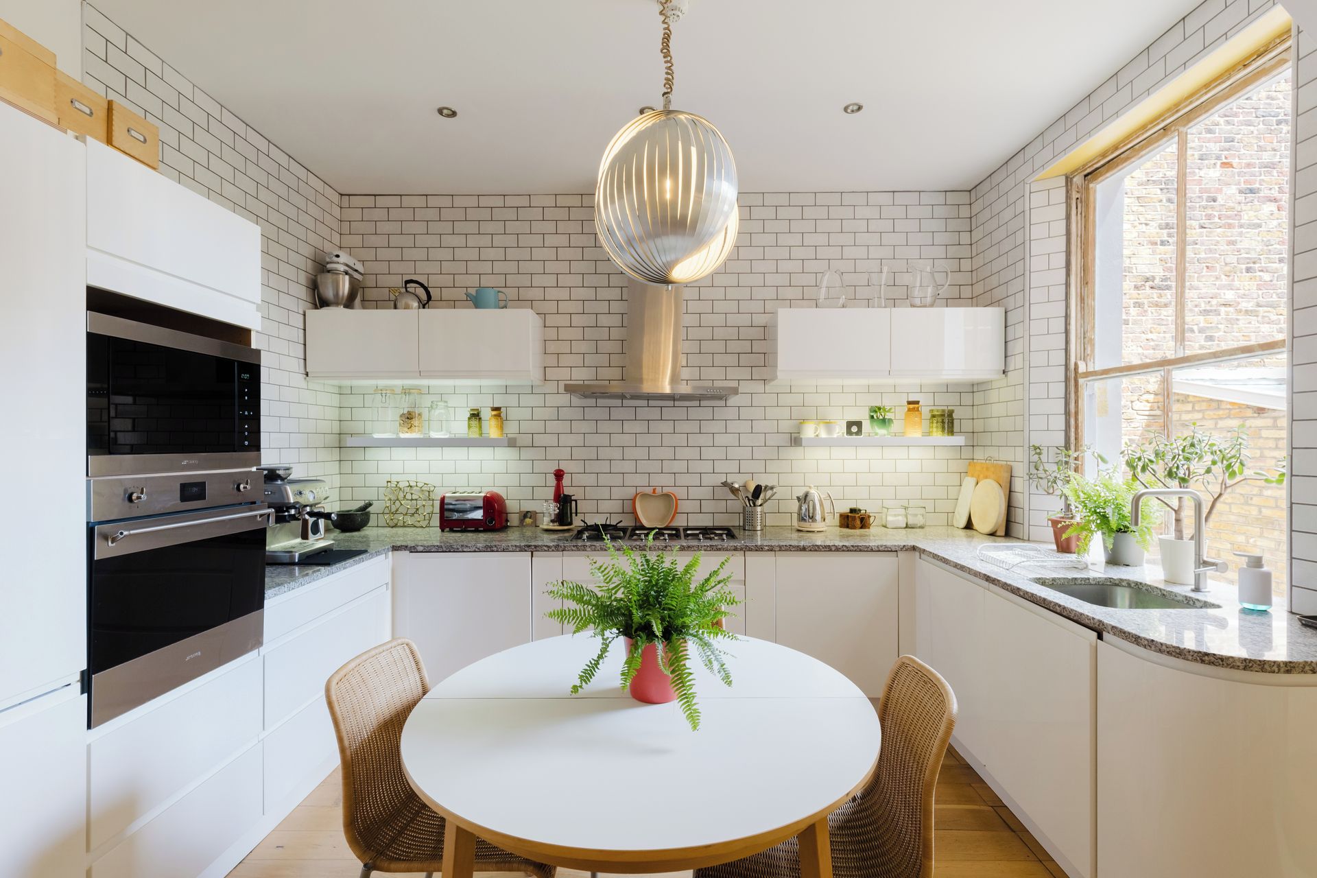 Une cuisine moderne avec des meubles blancs, une cuisinière en acier inoxydable et une table de salle à manger ronde entourée de chaises en osier.