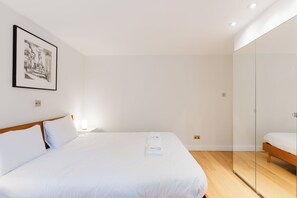 A modern bedroom with a large bed, a bedside table with a lamp, a framed picture on the wall, and a glass partition. - Colourful 3BDR Garden Maisonette in North London (Greater London)