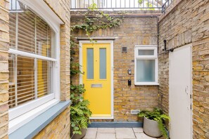 A narrow alleyway with a yellow door, a window with blinds, and a small window with a frosted glass pane. - Colourful 3BDR Garden Maisonette in North London (Greater London)