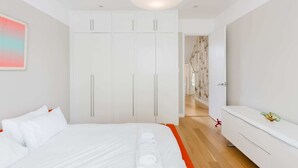 Un dormitori modern amb un llit, un armari blanc i un passadís que condueix a una altra habitació.