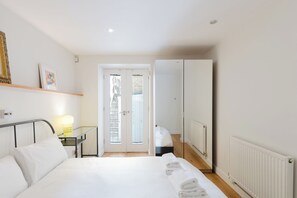 Ein Schlafzimmer mit Bett, Nachttisch, Lampe, Kleiderschrank und einer Tür, die auf einen Balkon führt.