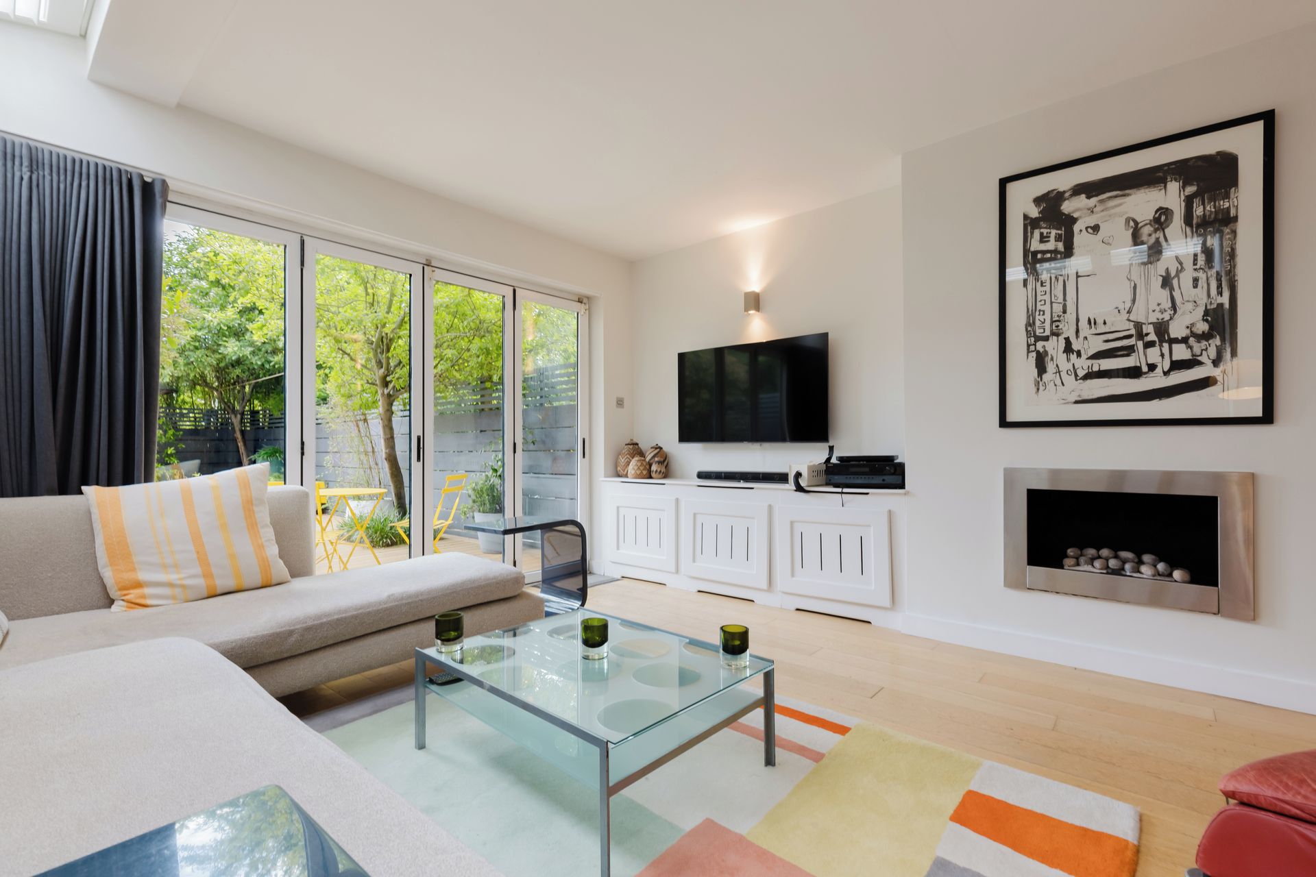 A modern living room with a sofa, a glass coffee table, a flat-screen TV, a fireplace, and a large framed artwork.