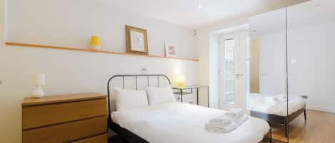 A bedroom with a bed, bedside table, lamp, and a mirror.