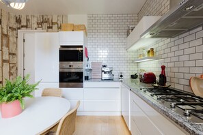 A modern kitchen with white cabinetry, a built-in oven, a coffee machine, and a gas stove. - Colourful 3BDR Garden Maisonette in North London (Greater London)