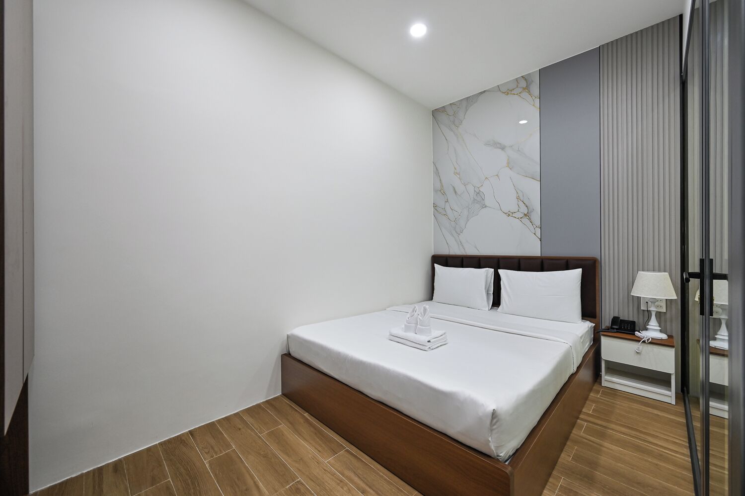 A modern hotel room with a large bed, a marble accent wall, and a bedside table with a lamp.