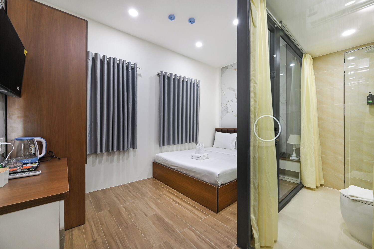 A hotel room with a bed, a coffee machine, a desk, and a shower area.
