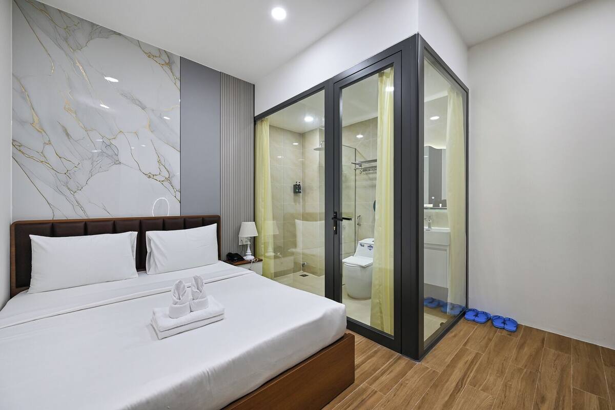 A hotel room with a bed, a glass-enclosed shower area, and a marble wall.