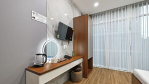 Habitación de hotel con un escritorio de madera, un espejo, una cafetera, un teléfono y un televisor montado en la pared.