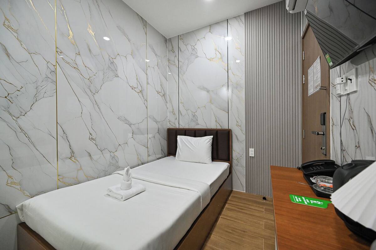A hotel room with a bed, a wooden side table, a telephone, and a wall with a marble pattern.
