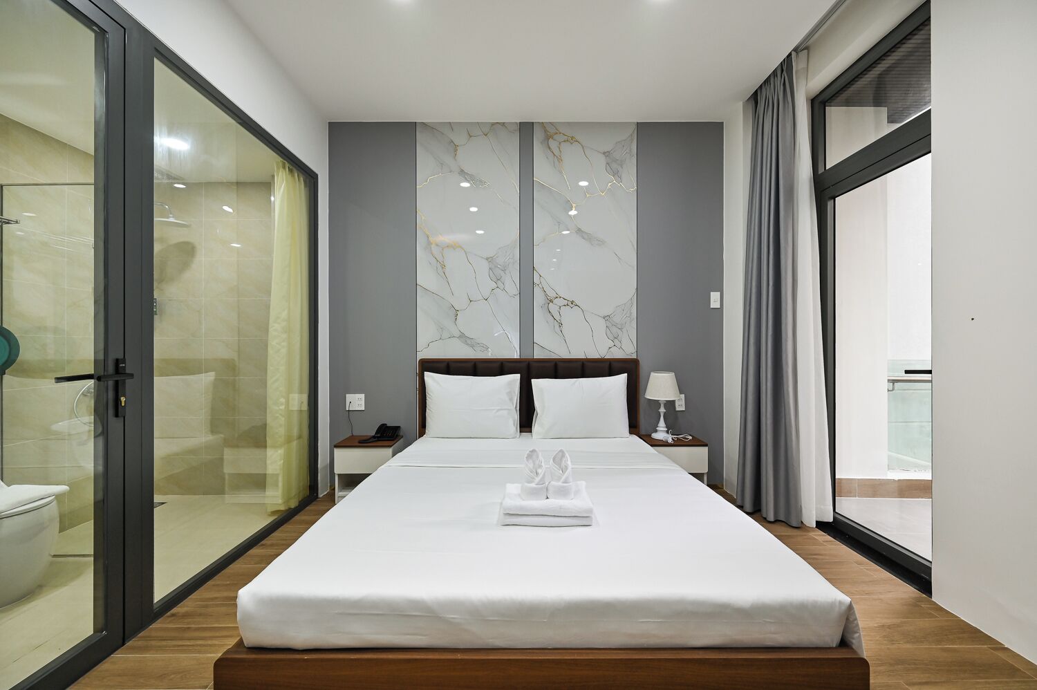 Ein Hotelzimmer mit einem großen Bett, einer Duschkabine aus Glas, einer Marmorwand und Blick durch ein Fenster.