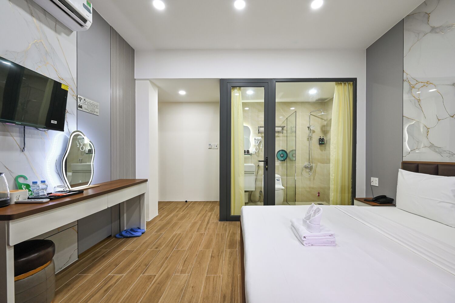 A hotel room with a bed, a desk with a mirror, a TV, and a shower area.