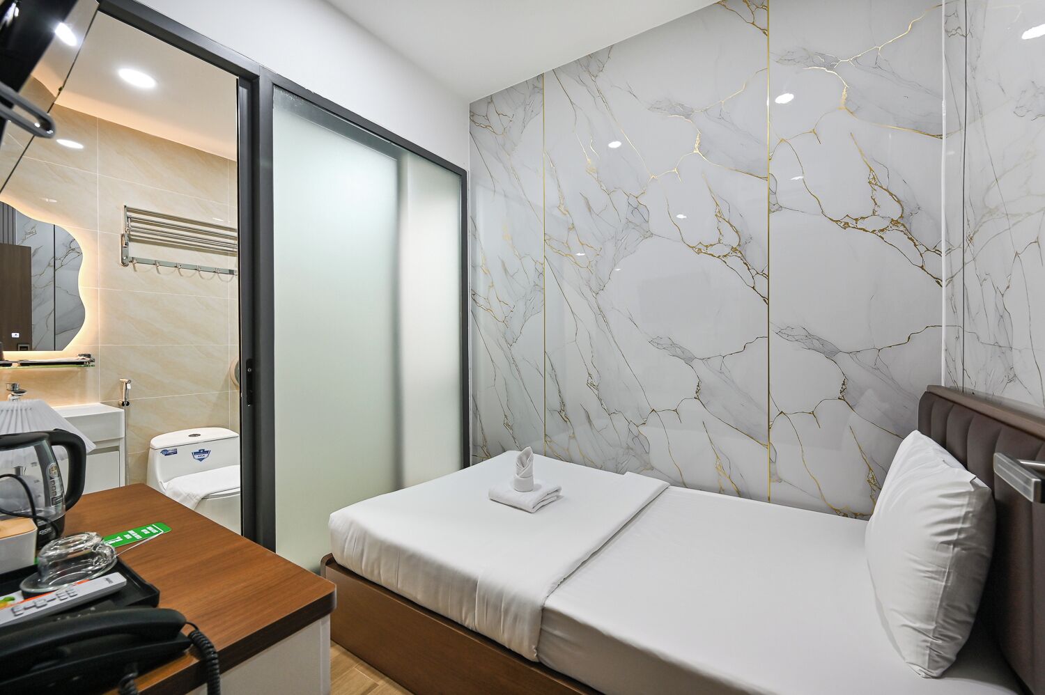 Ein Hotelzimmer mit einem Bett, einem Schreibtisch mit Telefon, einem Spiegel und einem Badezimmer mit Toilette und Waschbecken.
