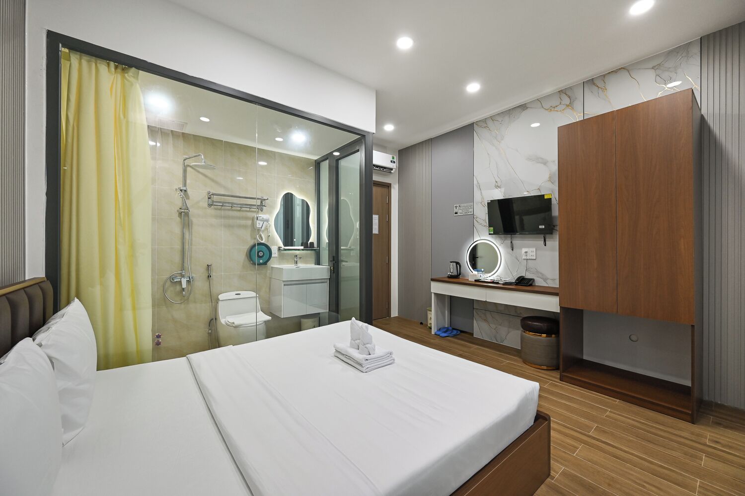 A hotel room with a bed, a bathroom with a shower, a vanity with a mirror, and a television.