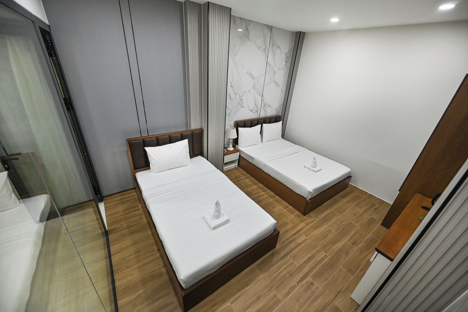 Ein modernes Hotelzimmer mit zwei Einzelbetten, Holzboden, einer Wand mit Marmorverkleidung und einer Glaseinteilung.