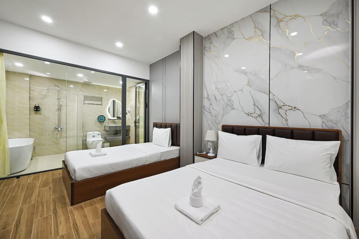 A hotel room with a large bed, a smaller bed, a shower area, and a marble wall.