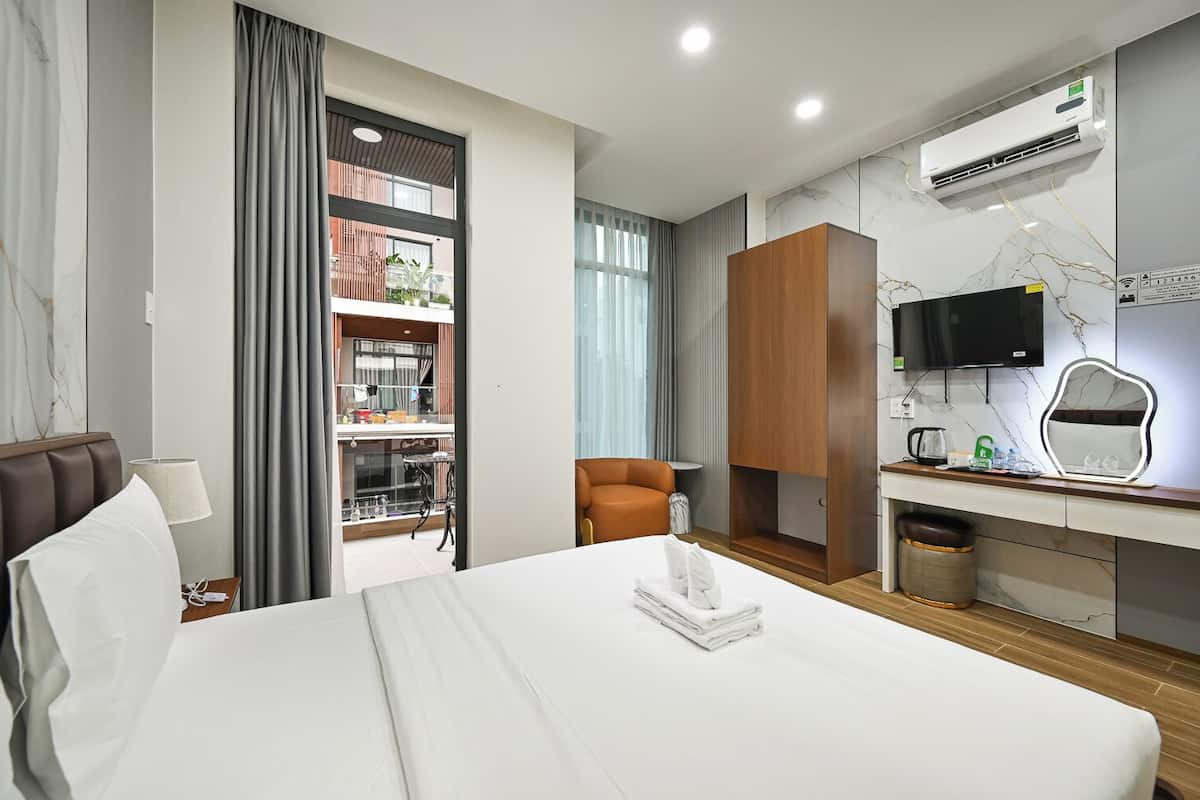 A hotel room with a bed, a desk, a chair, a TV, and an air conditioning unit.