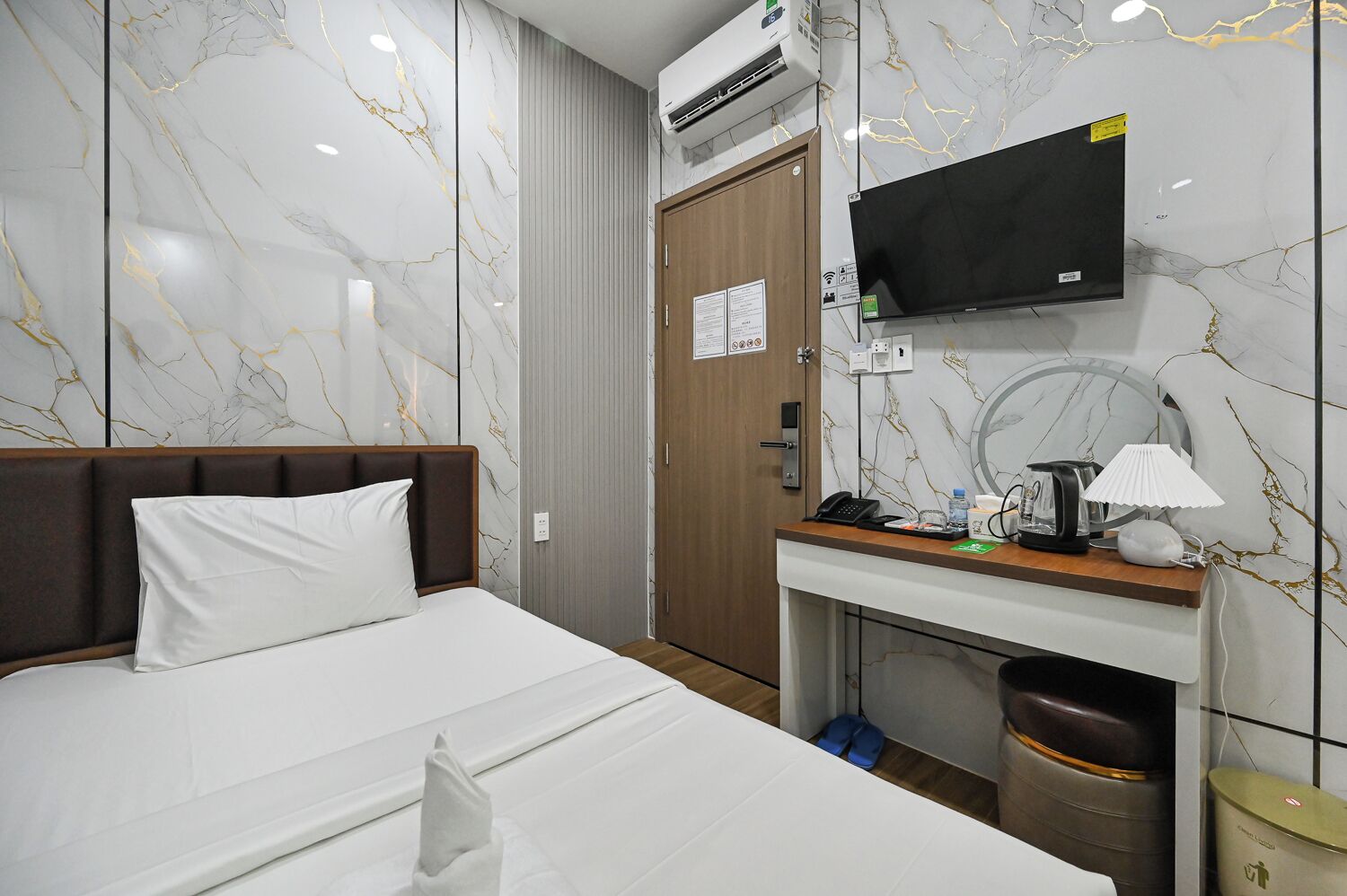 A hotel room with a bed, a desk with a telephone, a television, and a trash bin.