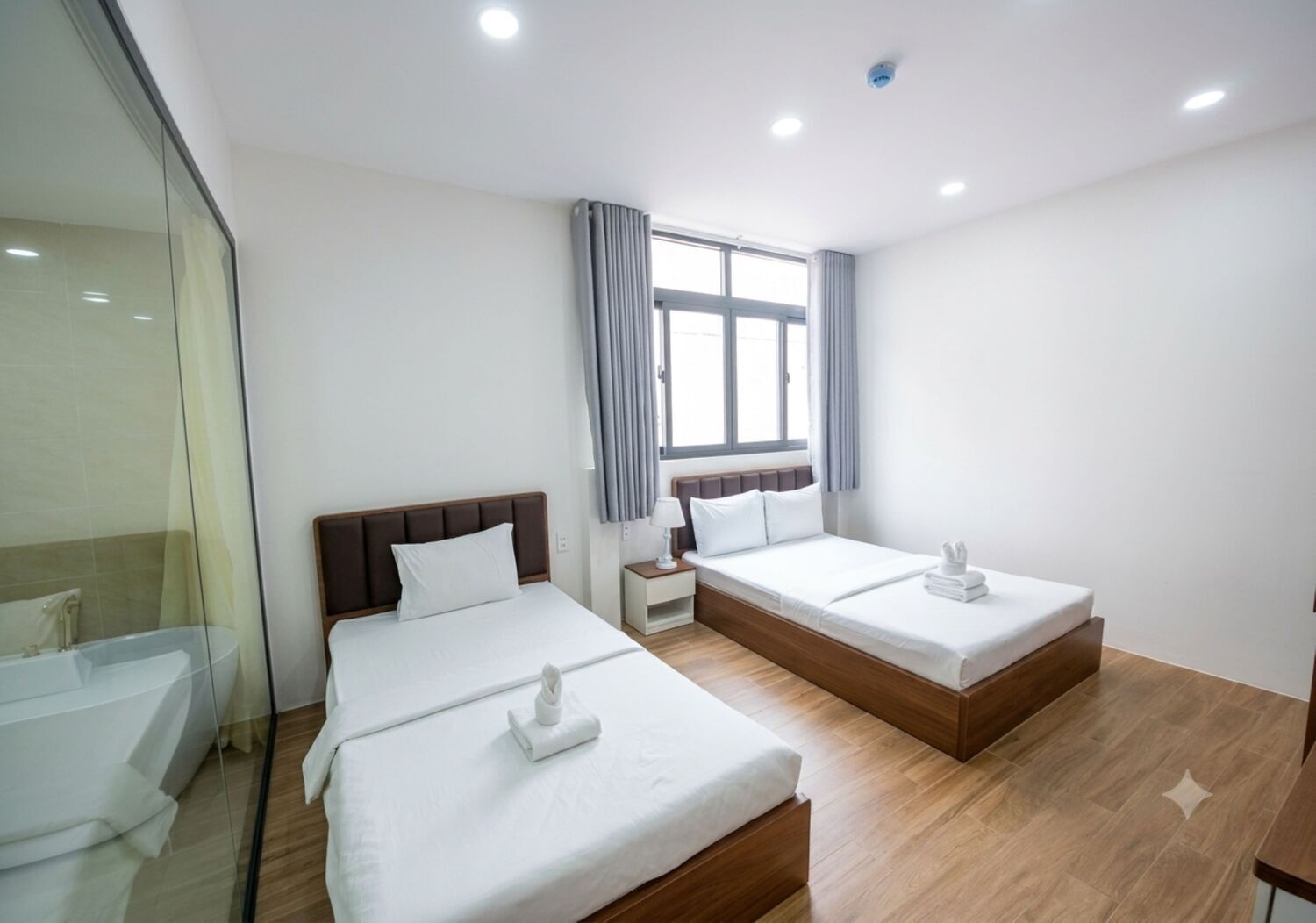 Une chambre d’hôtel avec deux lits, une salle de bain dotée d’une douche à parois de verre et une fenêtre avec des rideaux.