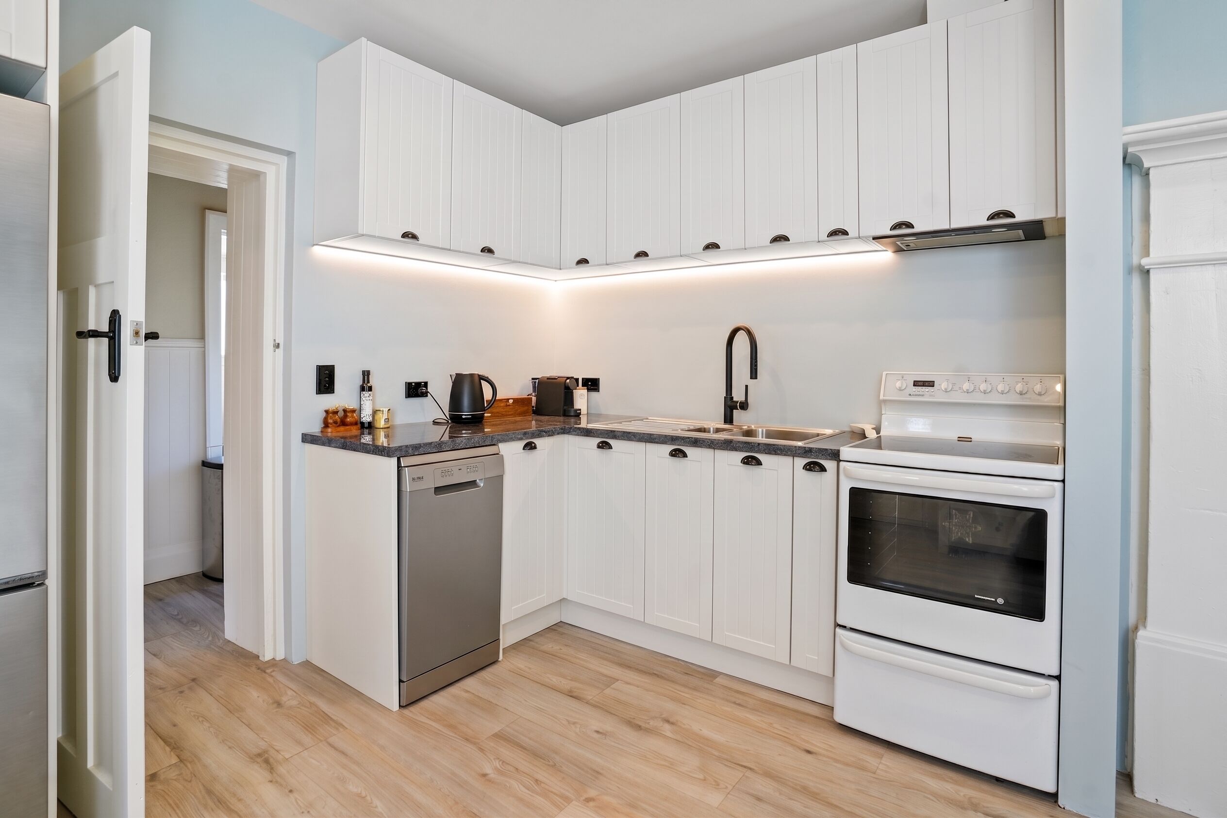 A kitchen with white cabinets, a dishwasher, a stove, and a sink.