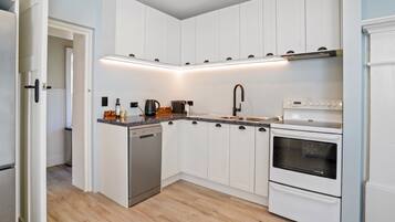 A kitchen with white cabinets, a dishwasher, a stove, and a sink.