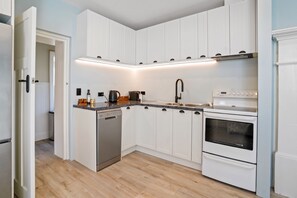 A kitchen with white cabinets, a dishwasher, a stove, and a sink.