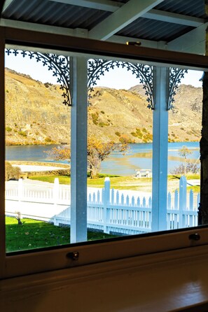 A view through a window with decorative metalwork, a white picket fence, and a river with hills in the background.