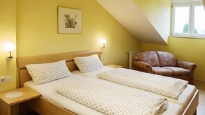 Ein Zimmer mit zwei Betten, einem braunen Ledersessel, einem Wandbild und einem Fenster mit Blick.