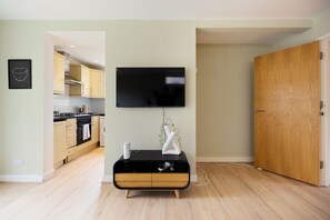 Een moderne woonruimte met een flatscreen televisie aan de wand, een houten kast met lades, en een houten deur.