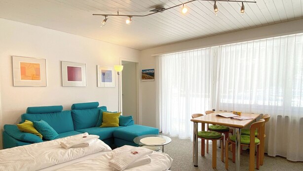 Una habitación con cama, sofá, mesa de comedor con sillas y una ventana con cortinas.